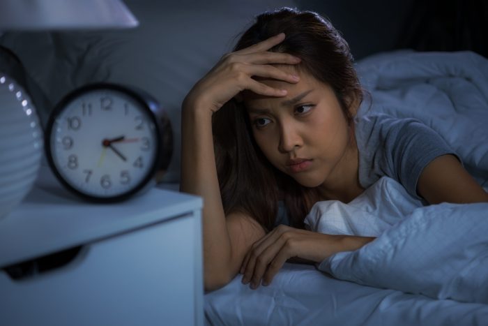 Woman experiencing insomnia, looking at alarm clock in a dark bedroom, emphasizing sleep difficulties and anxiety.