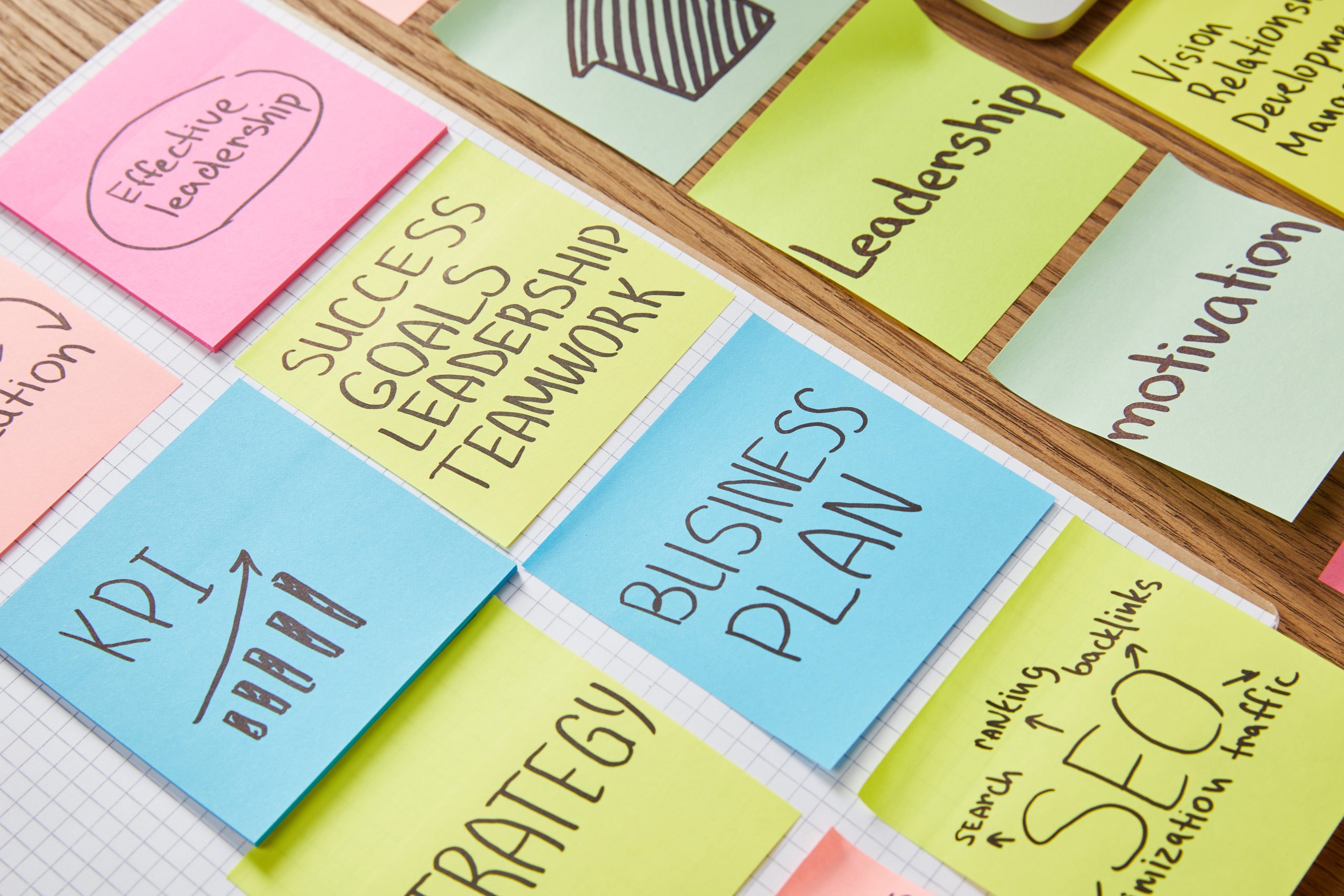 Colorful sticky notes displaying keywords related to business strategy, including "Effective leadership," "Success goals," "Business plan," and "SEO," arranged on a wooden surface.