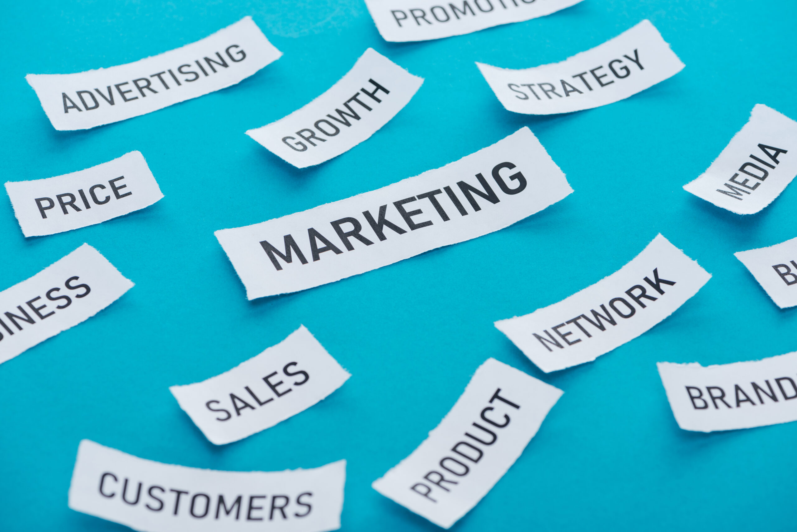 Marketing keywords on paper strips including "Advertising," "Growth," "Strategy," "Sales," "Customers," and "Product," arranged on a blue background, reflecting essential components of digital marketing strategies.