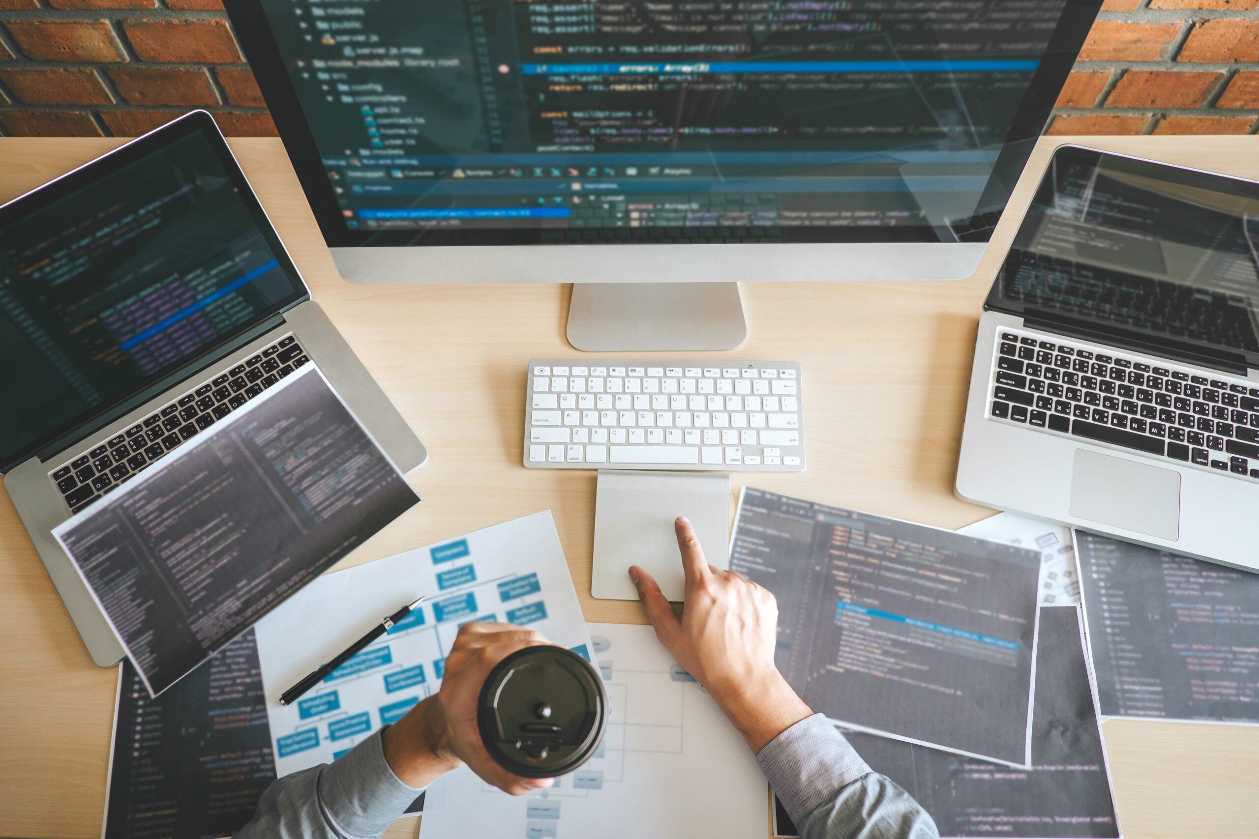 Professional developer working on software development with multiple laptops, computer screen displaying code, and documents related to website security and design.